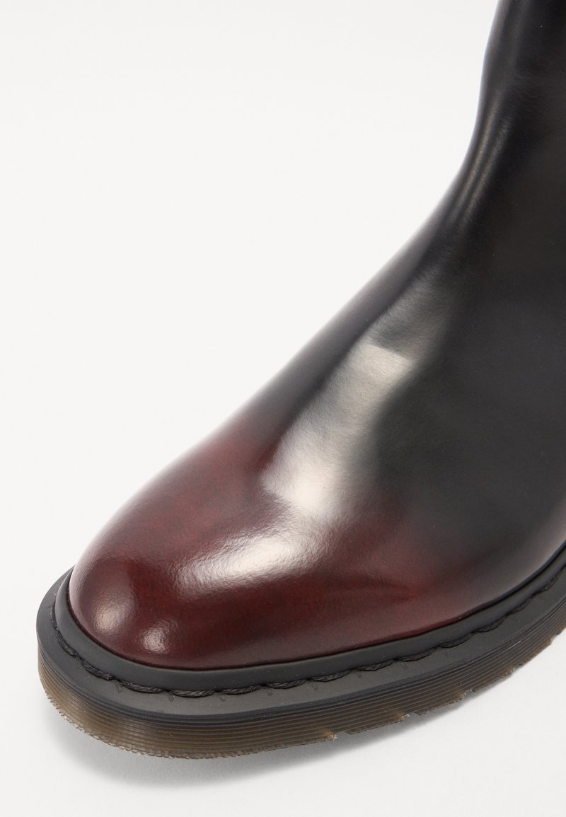 Botín de tobillo brillante de dos tonos con un upper de cuero rojo oscuro y negro, punta redonda y una suela de goma texturizada con detalles de costura.
