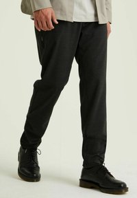 Schwarze, strukturierte Hosen mit entspanntem Schnitt, kombiniert mit polierten schwarzen Lederschuhen mit Flügelkappen-Details.