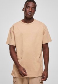Tricou din bumbac bej, cu decolteu rotund și mâneci scurte. Croială lejeră, cu o textură fină și un design simplu. Fără modele sau accente vizibile.
