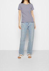 Pruhované tričko s krátkým rukávem, kulatým výstřihem a volánkovým lemem; nošeno s světle modrými džíny rovného střihu a bílými sandály.