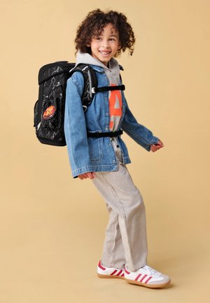 Black backpack with lightning pattern, denim jacket, gray hoodie, striped pants, and red and white sneakers, against a beige background.