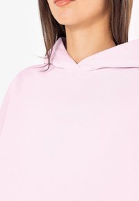 Sweatshirt com capuz rosa claro, com um corte descontraído. Apresenta um logo texturizado no peito e um tecido suave com um acabamento liso.
