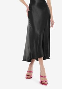 Vestido de satén negro con una silueta fluida y una abertura lateral, combinado con sandalias de tacón brillantes en color rosa con correas anchas.