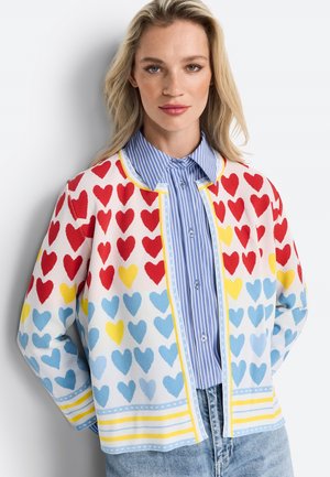 Strickjacke mit Herzmuster in Rot, Blau und Gelb auf einem weißen Hintergrund. Klassischer Kragen, offene Front und gerippte Akzente.
