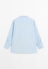 Camicia azzurra a manica lunga con polsini, mostrata da dietro su uno sfondo bianco, senza motivi o loghi visibili.