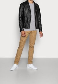Black leather biker jacket, gray t-shirt, tan chinos, and white sneakers. The jacket features zippers and a classic silhouette.