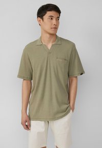 Oliwkowa koszulka polo z krótkim rękawem w ryflowanym wzorze, z dekoltem w kształcie litery V oraz kieszonką na piersi, w połączeniu z jasnymi szortami.