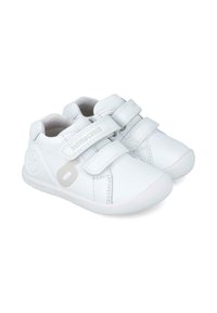 Zapatillas blancas de piel con doble tira de Velcro, puntera redondeada, suela de goma texturizada y detalle de logo en el lateral. Diseño limpio y minimalista.