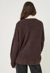 Pull oversized violet foncé avec un tricot texturé, des manches larges et un col rond, associé à un pantalon sombre.