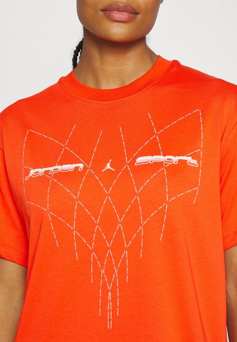 T-shirt en coton orange avec un col rond, arborant le texte blanc "Jordan" et "Sport", ainsi qu'un motif de couture géométrique blanc à l'avant.
