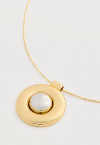 Zlatý obojkový náhrdelník s centrálnou bielou perlou na tenkej zlaté retiazke na bielom pozadí.