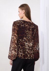 Blouse en imprimé léopard avec des manches longues et bouffantes ; tissu léger et fluide dans des tons de marron, beige et noir. Encolure arrondie dans le dos.
