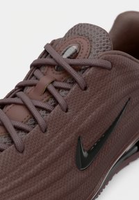 Nike sneaker egy tompa mályva színben, texturált hálós felsőrésszel, tonalitású fűzéssel és egy letisztult fekete logóval az oldalán.