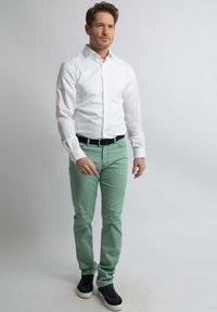 Weißes Hemd mit Knöpfen, kombiniert mit mintgrünen Hosen und schwarzen Sneakers. Das Outfit enthält einen schwarzen Gürtel und hat ein klassisches, figurbetontes Design.