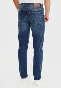 Niebieskie dżinsy o prostym kroju, z tylnymi kieszeniami i brązową skórzaną naszywką w talii. Czysty, klasyczny styl.