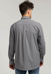 Czarna i biała koszula w kratę z kołnierzykiem, długimi rękawami, mankietami na guziki i karczkiem z tyłu. Wykonana z fakturowanej tkaniny.