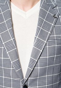 Granatowo-biała marynarka w kratę z wyłogami, o subtelnej fakturze i z pojedynczym czarnym guzikiem. Zakładana na jasny sweter z dekoltem w serek.