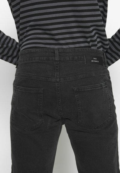 Jean en denim noir avec une texture lisse, présentant un design classique à cinq poches et une petite étiquette à l'arrière de la taille.