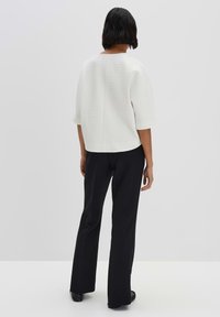 Top bianco con texture e maniche corte, abbinato a pantaloni neri a gamba dritta. Design semplice, vestibilità rilassata e linee pulite.