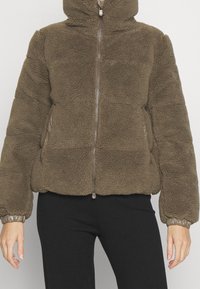 Hnědá měkká fleecová bunda s kapucí, předním zipem a elastickými manžetami. Má boční kapsy, volný střih a texturovaný povrch.