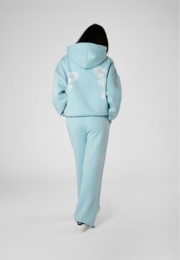 Set di felpa e pantaloni della tuta di colore azzurro chiaro, realizzato in materiale morbido, con vestibilità oversize e motivi astratti bianchi sulla schiena e sulle gambe.