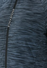 Blå atletisk jacka i lätt, texturerad tyg med ett subtilt randigt mönster, med en svart dragkedja och "ENDURANCE"-logotyp.