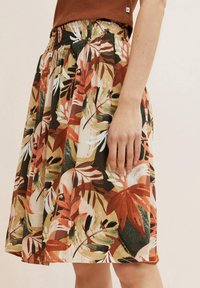 Jupe florale avec une taille smockée et un mélange de tons terreux, ornée de grands motifs de feuilles vertes, rouges et blanches sur un fond clair.