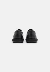 Scarpe in pelle nera con finitura testa di moro, punta arrotondata e suola imbottita. La vista posteriore mostra dettagli di cucitura semplice e un design a profilo basso.