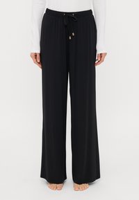 Μαύρο παντελόνι με φαρδύ πόδι, κατασκευασμένο από ελαφρύ ύφασμα, διαθέτοντας ελαστική μέση με κορδόνι και χρυσές μεταλλικές λεπτομέρειες. Χωρίς τσέπες.