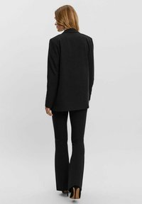 Blazer nero con vestibilità rilassata, abbinato a pantaloni neri a zampa d'elefante. Tessuto morbido e maniche lunghe. Scarpe con tacco completano l'outfit.