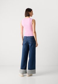 En rosa, ribbet uten ermer topp sammen med vid ben blå denimbukser med frynsete kant og grå mansjetter. Modellen står med ryggen til.