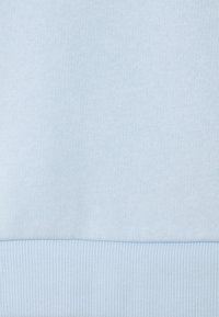 Ljust blått bomullstyg med en mjuk textur. Har en ribbad ärm vid botten, vilket ger en ren och slät yta överlag.