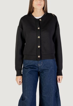 Zwarte cropped sweatshirts met ronde halslijn, sluiting met knopen aan de voorkant en metalen knopen, gecombineerd met denim jeans met wijde pijpen.