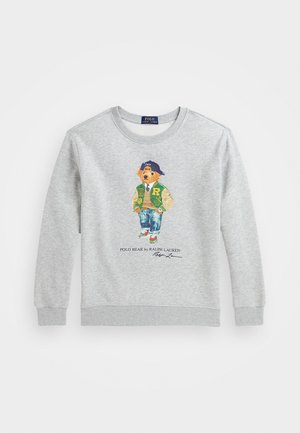 Felpa grigia con polsini e girocollo a coste. Presenta un orso illustrato che indossa una giacca varsity verde, jeans e un berretto blu.