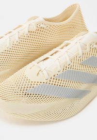 Baskets légères beige avec un design en treillis 3D et trois bandes diagonales grises sur les côtés.