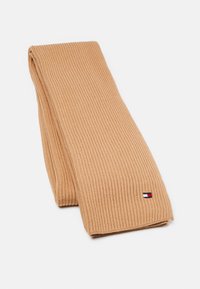 Écharpe beige côtelée en matière douce, ornée d'un petit patch logo rouge, blanc et bleu. Vue à plat mettant en valeur sa longueur et sa texture.