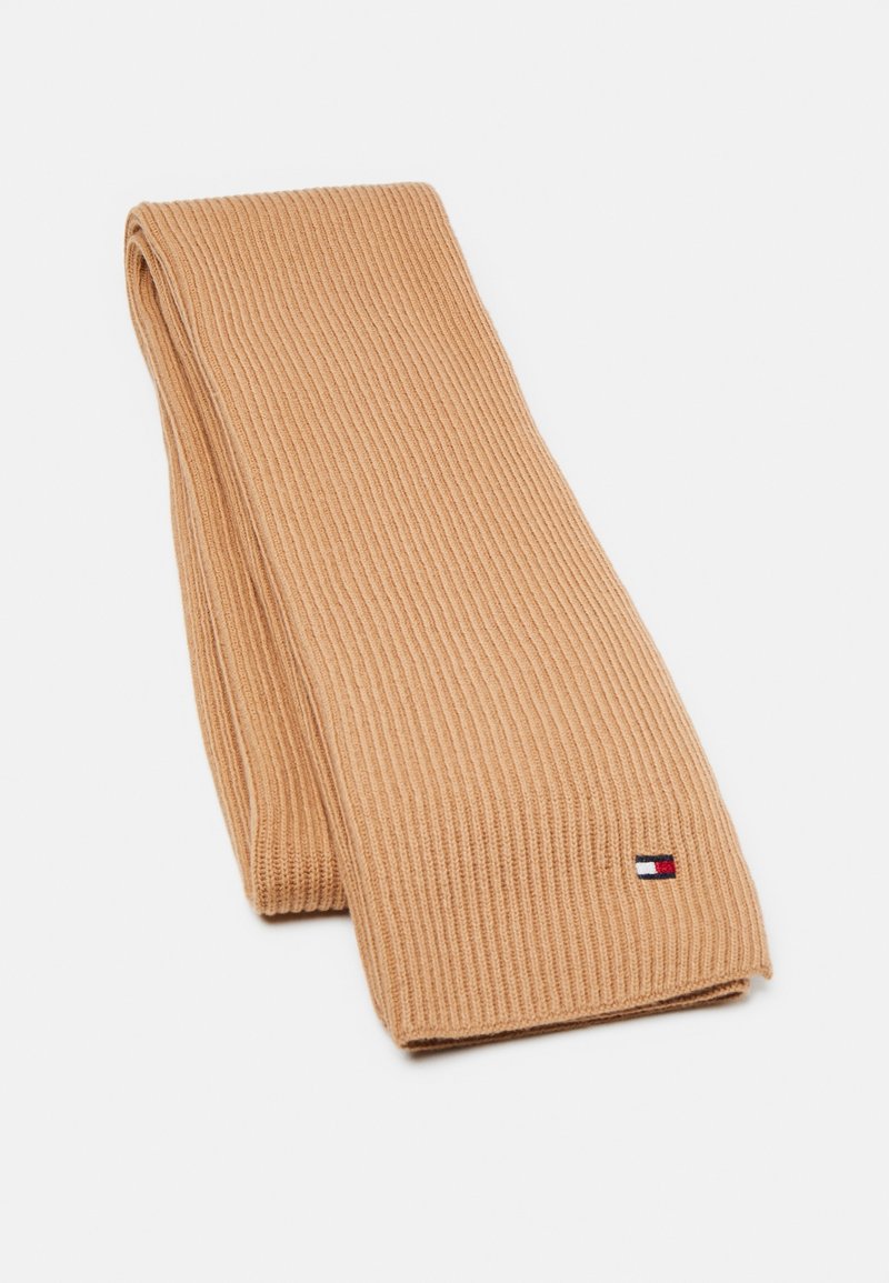 Écharpe beige côtelée en matière douce, ornée d'un petit patch logo rouge, blanc et bleu. Vue à plat mettant en valeur sa longueur et sa texture.