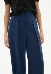 Marineblaue, plissierte Hosen aus glattem Stoff, mit hoher Taille und seitlichen Taschen, in lockerer Passform für optimalen Komfort gestaltet.