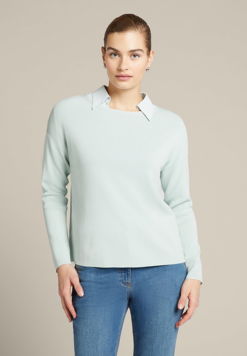 Helles mintgrünes Sweater mit rundem Halsausschnitt und kontrastierendem weißen Kragen. Weiche Textur, lange Ärmel und lässige Passform. Kombiniert mit blauen Jeans.