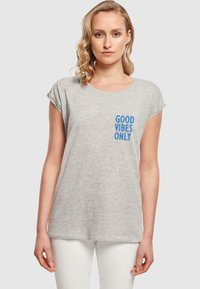 Grå bomull t-skjorte med rullet erme, med blå tekst "GOOD VIBES ONLY" på venstre brystområde. Enkel, avslappet passform.