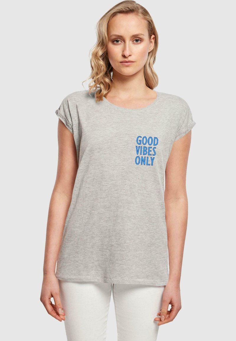 Grå bomull t-skjorte med rullet erme, med blå tekst "GOOD VIBES ONLY" på venstre brystområde. Enkel, avslappet passform.