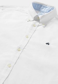 Biała koszula na guzik z bawełny, z jasnoniebieskim wykończeniem kołnierza, żółtymi guzikami i małym ciemnym logo na lewej piersi.