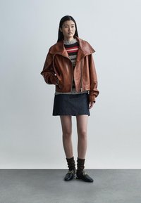 Pruun nahast lühike jakk ülisuurte kraedega, halli ja punase triibulise mustriga kootud kampsun, tume teksaseelik ja mustad kingad kuldsete detailidega.