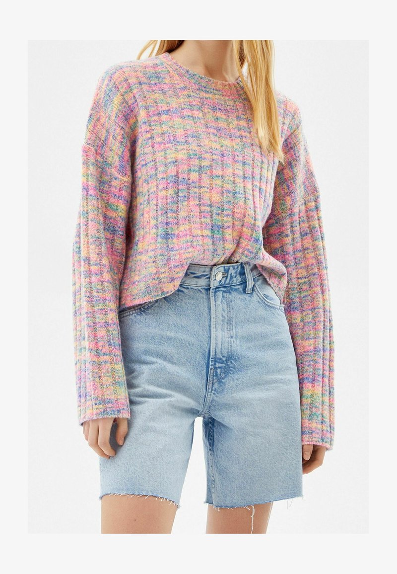 Femme portant un pull en tricot pastel multicolore rentré dans un short en jean délavé clair taille haute avec ourlet brut.