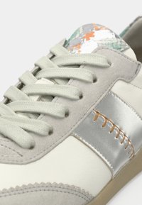 Hellgrauer Sneaker mit einer strukturierten Oberseite aus Wildleder, silbernen Akzenten, hellgrünen Schnürsenkeln und einem gemusterten, farbenfrohen Detail in der Nähe der Zunge.