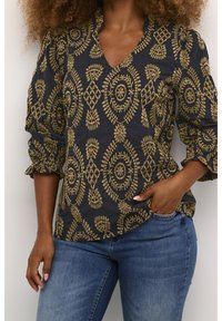 Svart blus med gyllene blommig broderi, V-ringad naken och puffärmar; matchat med blå jeans.