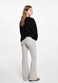 Svart blus med puffärmar och plisserad rygg, i kombination med ljusgrå flare jeans med fransade nederkanter.