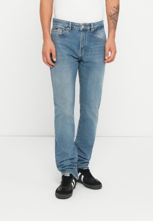 Vaqueros de mezclilla azul claro con corte recto, que cuentan con cinco bolsillos y cierre de botón. Llevados con zapatillas negras y una camiseta blanca.