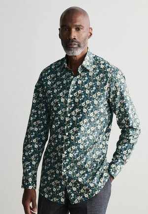 Camicia a bottoni floreale in tessuto verde scuro, con fiori bianchi e beige, maniche lunghe e un design con colletto classico. Finitura testurizzata.