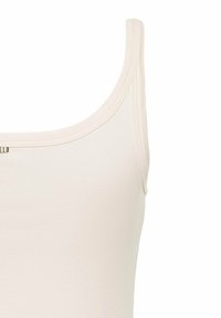 Light beige tank top featuring a rounded neckline, thin straps, and a smooth cotton blend texture. Includes a small logo accent beneath the neckline.